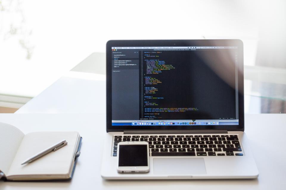 A laptop showing code with a phone on the keyboard
